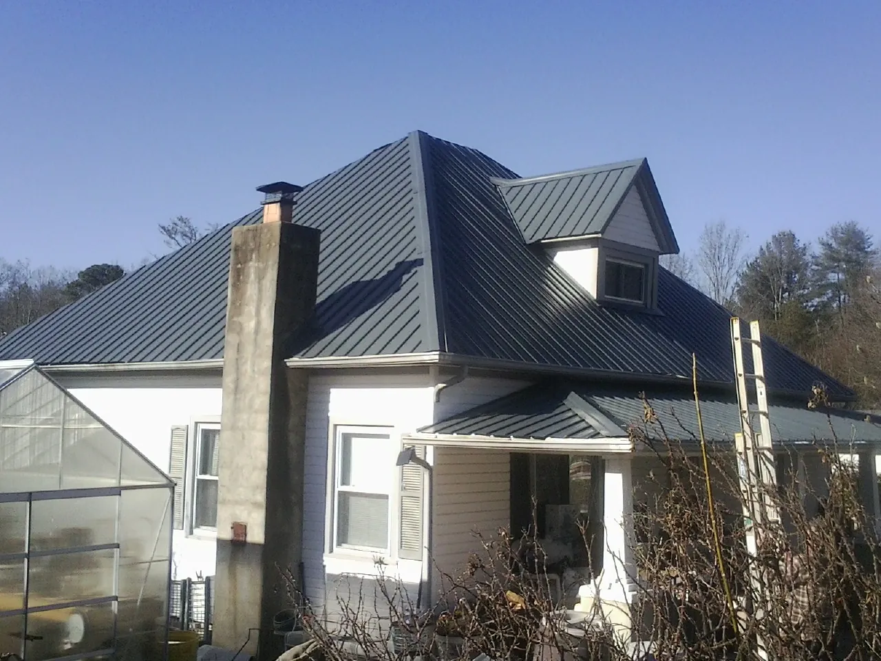 Dark blue standing seam metal roof on a white farmhouse with dormer — Slate & Tile Roof Repair by Roofing Brothers in Modena
