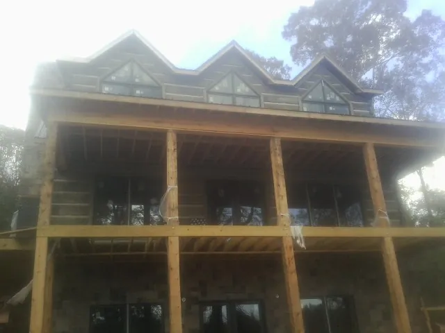Dormers and porch framing on a large log home under construction — Roof Coating work by our crew in Modena